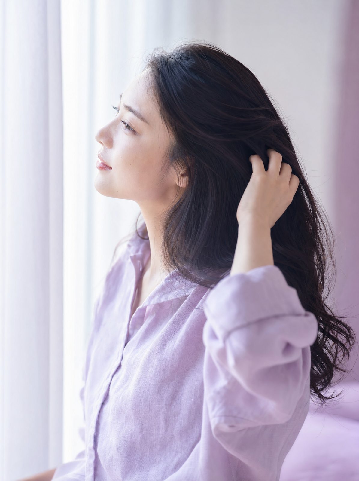 窓辺で髪に指を通す女性